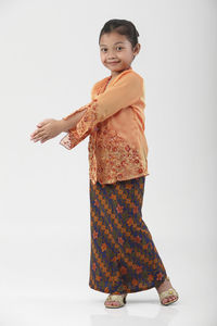 Portrait of cute teenage girl wearing traditional clothing dancing against white background