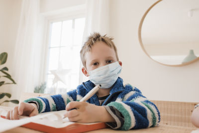 Boy home schooling with a medical mask on to protect from a virus