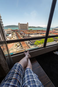 Low section of man relaxing in city against sky