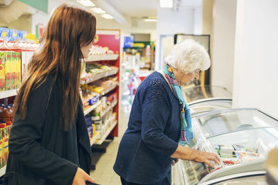 Young woman looking at grandmother shopping in supermarket