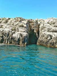 Rock formations by sea against clear blue sky