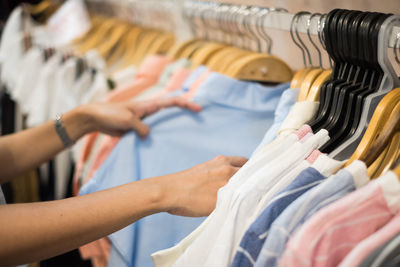 Cropped hands of woman choosing tops in clothing store