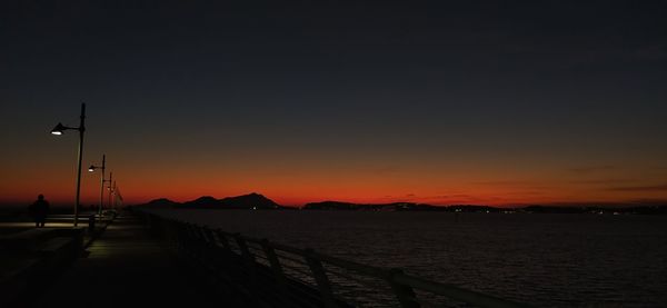 Silhouette street by sea against sky during sunset