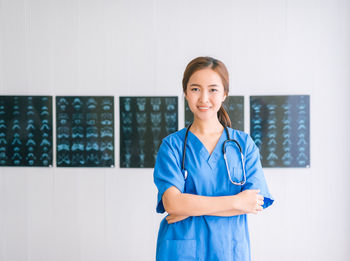 Portrait of female doctor smiling while standing against x-rays on wall