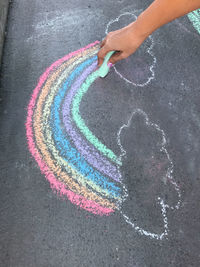 Cropped hand of woman drawing rainbow on footpath