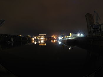 Illuminated commercial dock by sea against sky at night