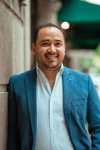 Hispanic mature male entrepreneur looking away while leaning on shabby wall on aged building in city