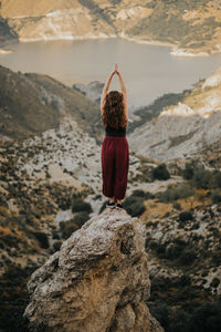 Rear view of woman with hands clasped standing on rock formation