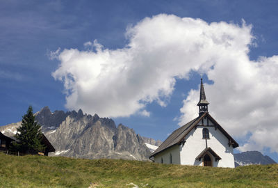 Traditional windmill on field by building against sky