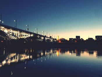 Illuminated bridge over river by buildings against sky during sunset