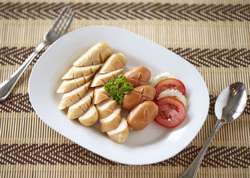 High angle view of sausages with vegetable slices in plate on table