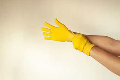 Hands put on yellow gloves for repair, painting the walls, diy on the background of an empty wall.