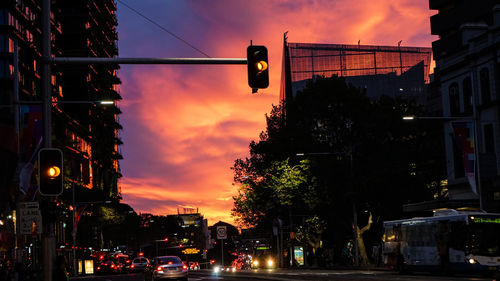 Illuminated road signal in city against orange sky