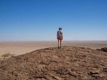 Rear view of young woman standing on desert rock against clear blue sky, namib naukluft national park, namibia