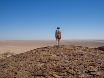 Rear view of man standing on desert against clear blue sky