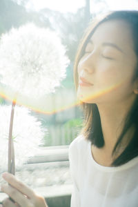 Woman with closed eyes by dandelion in sunny day