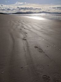 Footprints on wet sand at beach against sky