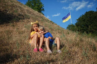 Girl in yellow and boy in blue near biggest national flag of ukraine. pray for peace and victory
