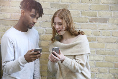 Young man using mobile phone against wall