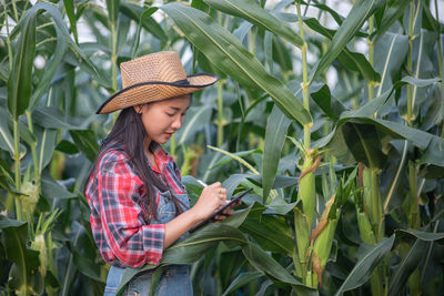 Woman using digital tablet while examining plants on agricultural field