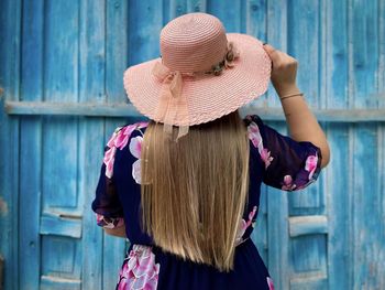 Rear view of blonde woman wearing pink dress and hat facing a blue wooden door