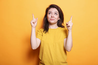 Young woman gesturing against yellow background