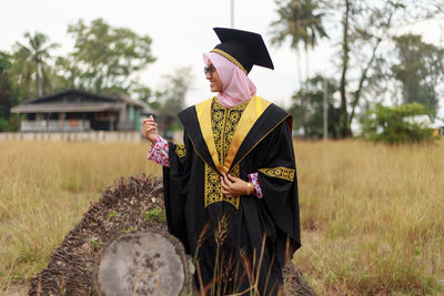 Woman in graduation gown standing by log