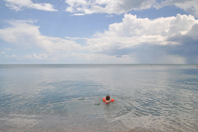 Child swimming in sea against cloudy sky