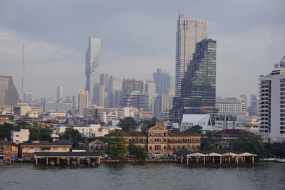 Buildings by river against sky in city