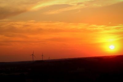 Silhouette of wind turbines on land against sky during sunset