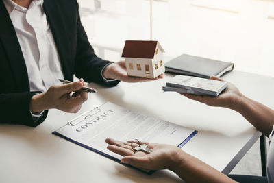 Midsection of agent with model home and customer holding key and money