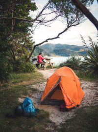 Orange tent at campsite with woman making coffee in background