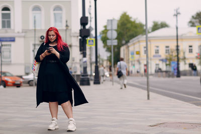 Full length of woman standing on mobile phone in city