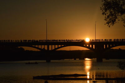 Silhouette people on bridge over river against sky during sunset