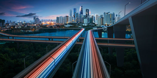 Light trails on bridge amidst buildings in city at night