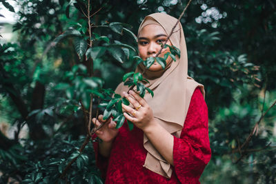 Portrait of young woman standing against plants