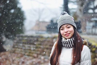 Portrait of beautiful woman standing on field during snowfall