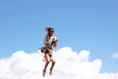 Low angle view of woman jumping against blue sky