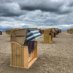Hooded chairs on beach against cloudy sky