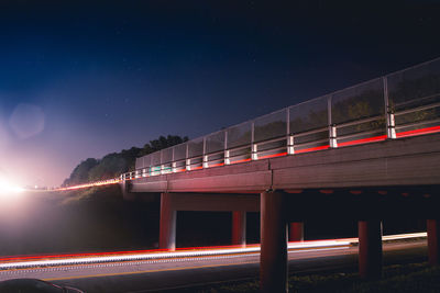 Light trails on bridge against sky at night