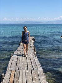 Young woman walking on pier over sea against sky