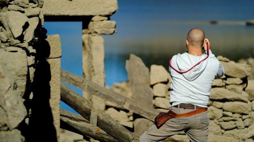 Rear view of man standing by stone wall during sunny day