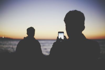 Silhouette people photographing sea against sky during sunset