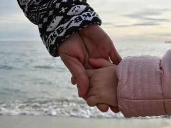 Cropped image of father holding child hand at beach