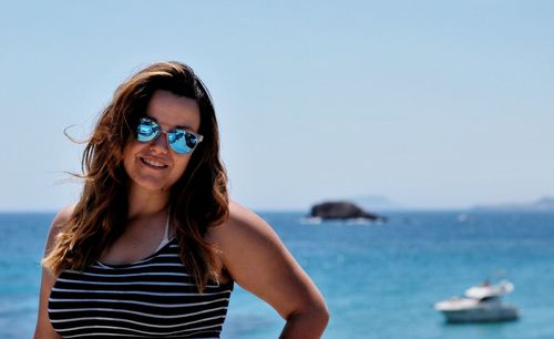 Portrait of smiling young woman standing at beach against clear sky