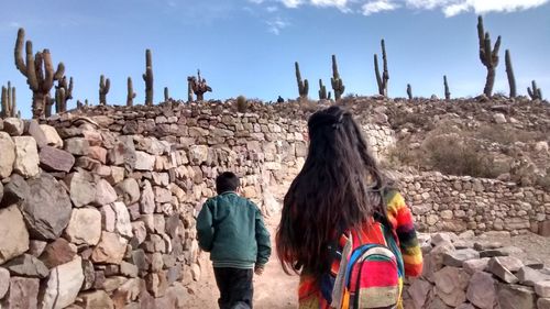 Rear view of friends standing on rock against sky