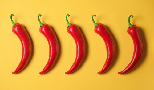 Five hot red peppers on a yellow background