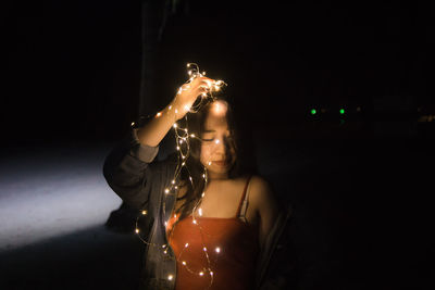 Portrait of woman with illuminated lighting equipment against black background