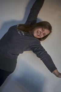 Portrait of smiling young woman stretching arms while standing against wall