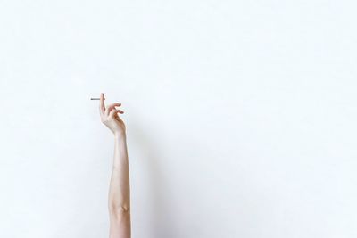 Low angle view of hand holding cigarette against white background